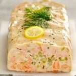 Terrine de poisson maison aux légumes, poisson blanc et saumon, coupée en tranches fraîches, servie avec sauce citronnée et herbes fraîches.