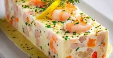 Terrine de poisson blanc et crevettes servie en tranches avec sauce citronnée, ciboulette fraîche, quartiers de citron et crevettes entières.