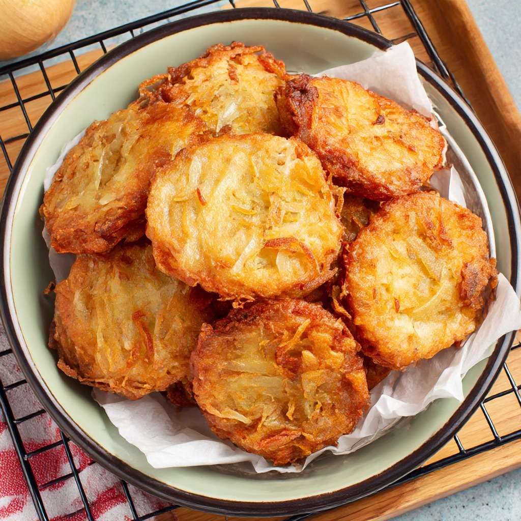 Beignets d’oignons croustillants dorés à la poêle, préparés avec une pâte légère à la farine, œuf, eau et levure, servis chauds.