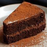 Gâteau au yaourt chocolaté coupé en parts, garni d’une ganache au chocolat noir lisse et saupoudré de cacao en poudre.