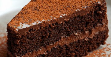 Gâteau au yaourt chocolaté coupé en parts, garni d’une ganache au chocolat noir lisse et saupoudré de cacao en poudre.