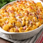 Gratin de coquillettes au jambon et gruyère râpé bien doré, servi chaud dans un plat familial avec une texture crémeuse.
