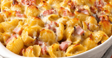 Gratin de coquillettes au jambon et gruyère râpé bien doré, servi chaud dans un plat familial avec une texture crémeuse.