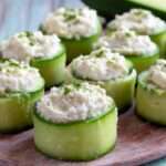 Bouchées de concombre garnies de fromage frais crémeux aux herbes, servies bien fraîches sur une assiette avec ciboulette et poivre.