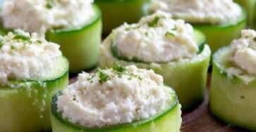 Bouchées de concombre garnies de fromage frais crémeux aux herbes, servies bien fraîches sur une assiette avec ciboulette et poivre.