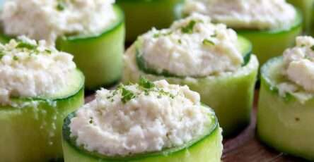 Bouchées de concombre garnies de fromage frais crémeux aux herbes, servies bien fraîches sur une assiette avec ciboulette et poivre.