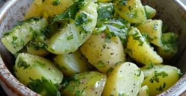 Salade de pommes de terre tièdes aux herbes fraîches servie dans un saladier, avec persil, ciboulette, échalote et vinaigrette maison.
