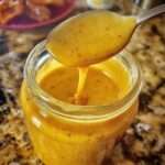 Vinaigrette miel-moutarde maison servie dans un petit pot en verre, avec une texture épaisse, brillante et dorée.