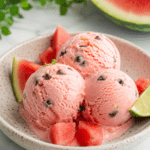 Boules de glace rose à la pastèque servies dans un bol froid, avec des pépites de chocolat rappelant les graines du fruit et des morceaux de pastèque fraîche.