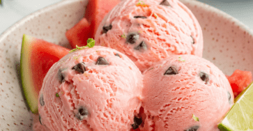 Boules de glace rose à la pastèque servies dans un bol froid, avec des pépites de chocolat rappelant les graines du fruit et des morceaux de pastèque fraîche.