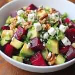 Salade colorée de betterave, avocat, feta et noix servie dans un grand saladier, avec herbes fraîches et vinaigrette brillante.