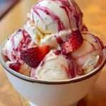 Boules de glace vanille crémeuse servies avec un coulis de fraises brillant, des morceaux de fraises fraîches et un effet marbré gourmand.