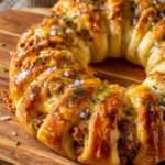Couronne feuilletée dorée garnie de viande hachée épicée et de fromage fondant, servie avec une sauce crémeuse au centre.