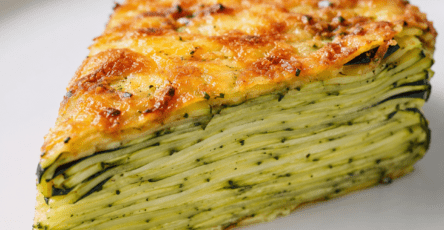 Gâteau invisible salé aux courgettes coupé en parts épaisses, montrant de nombreuses fines couches de légumes fondants liées par une pâte légère aux œufs et au parmesan, avec une surface dorée.