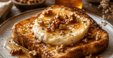 Tranches épaisses de pain perdu dorées à la poêle, garnies de chèvre frais légèrement gratiné, d’un filet de miel brillant, de thym et de noix concassées.