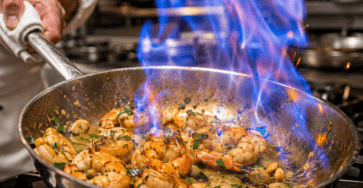 Crevettes au pastis roses flambées au pastis dans une poêle, enrobées d’une sauce brillante à l’ail, au persil et aux herbes provençales, servies avec du citron.