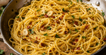Spaghetti aglio e olio brillants servis dans une poêle, garnis de fines lamelles d’ail doré, de piment rouge, de persil frais et d’huile d’olive.